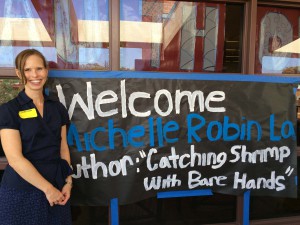 Michelle Robin La standing by a welcome poster for her talk at FHS