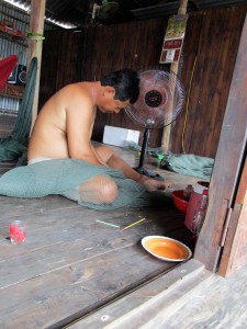 A fisherman repairing a net while sitting on the floor of his house in rural Vietnam.